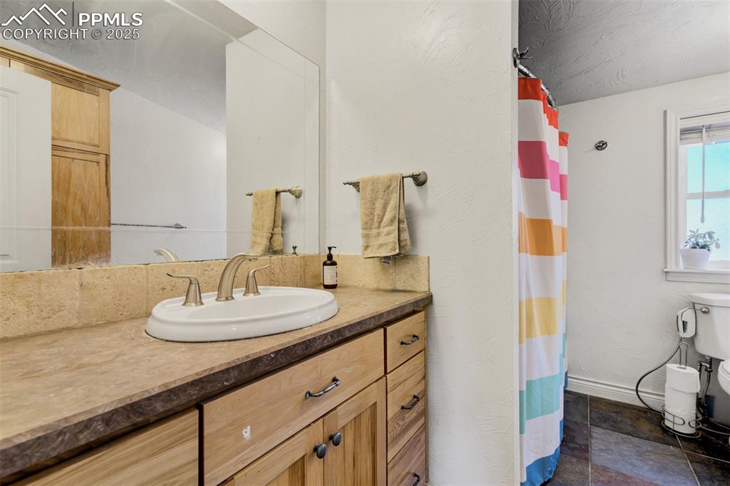 Image 34 of 50: Bathroom featuring toilet, a shower with curtain, stone finish floor, and v