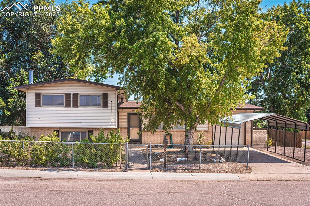 Caption: Split level home with a fenced front yard, brick siding, driveway, an attached garage, and a carport