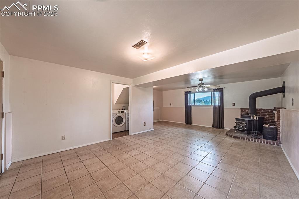 Image 11 of 31: ceiling fan, a wood stove, and light tile patterned flooring