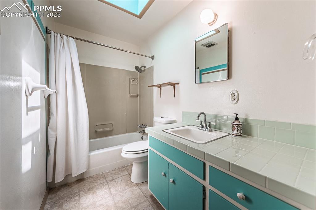 Image 18 of 31: Bathroom featuring a skylight, shower / bathtub combination with curtain, v