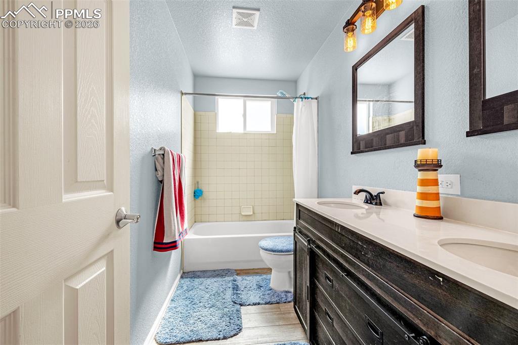 Image 16 of 40: Bathroom featuring a dual-sink vanity with white countertops, a dark wood-f