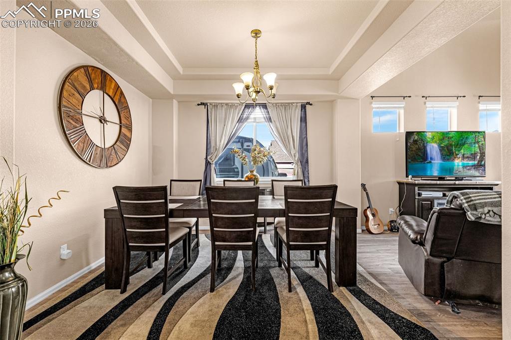 Image 5 of 40: Dining area featuring a tray ceiling with a brass chandelier, an accent wal