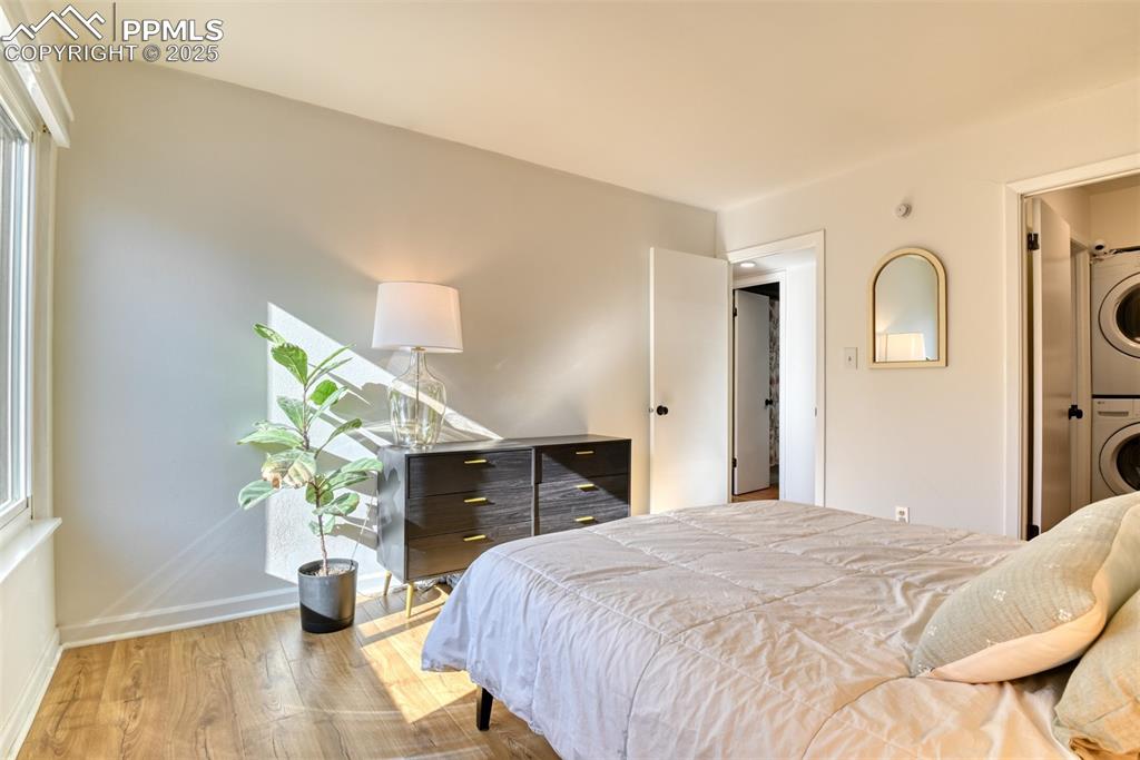 Image 25 of 31: Bedroom featuring wood finished floors, estacked washer and dryer, and ensu