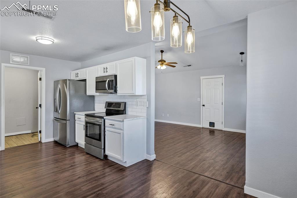 Image 7 of 22: Kitchen featuring white cabinetry, stainless steel appliances, dark wood-st
