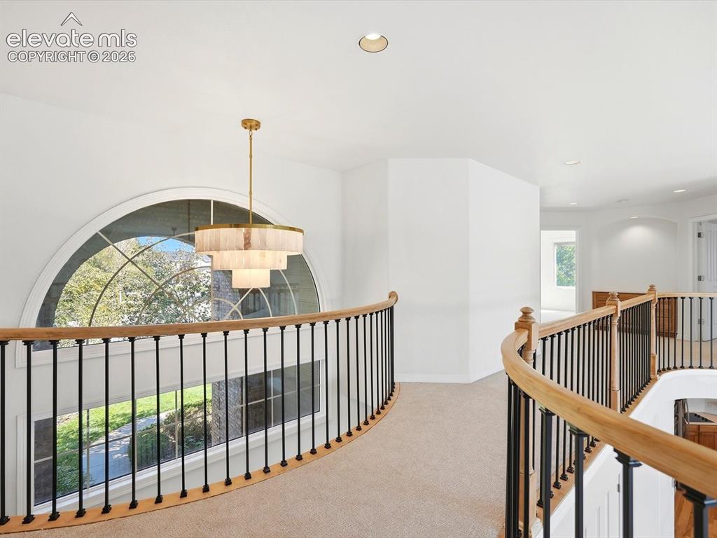 Image 25 of 48: Curved mezzanine gallery featuring a tiered brass chandelier, arched floor-