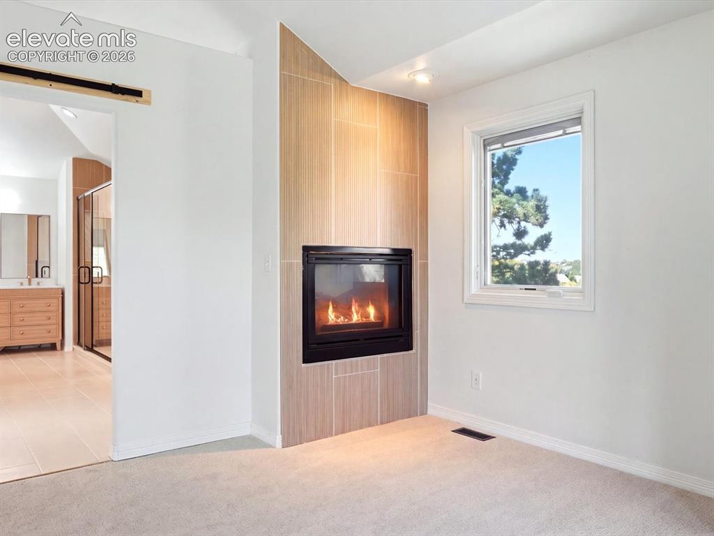 Image 28 of 48: Fireplace featuring floor-to-ceiling neutral tile surround, black metal fir