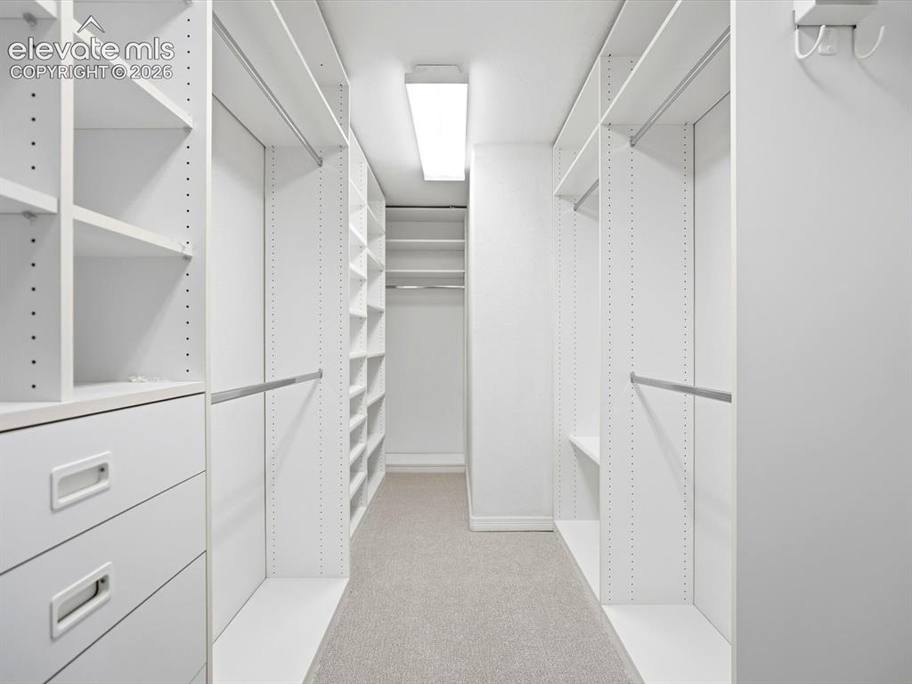 Image 31 of 48: Walk-in closet featuring white custom built-in shelving, hanging rods, inte