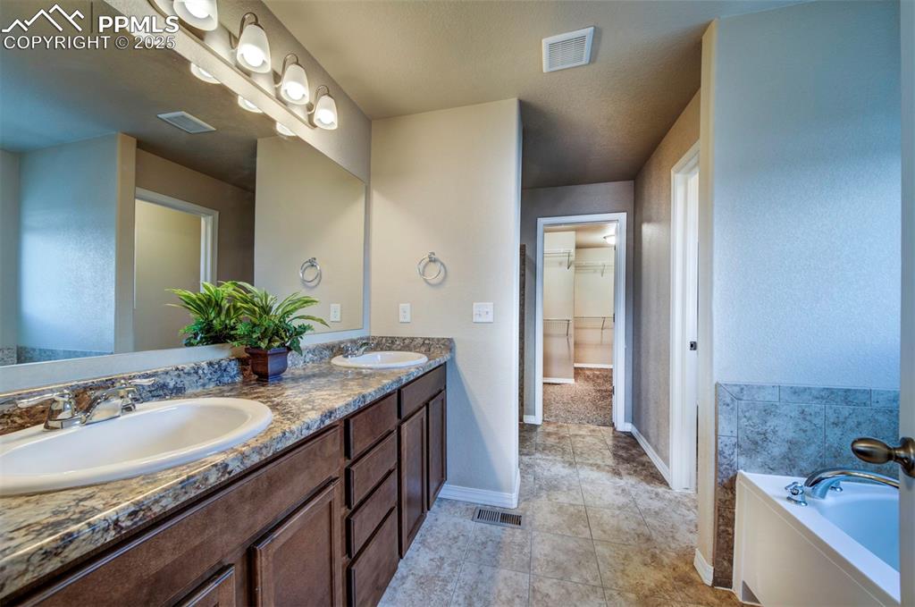 Image 24 of 46: Bathroom featuring double vanity, a bath, a spacious closet, and tile patte