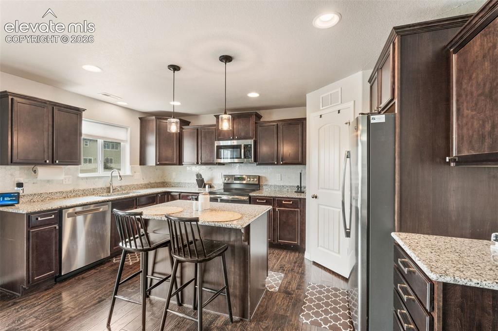 Image 16 of 42: Kitchen featuring dark wood-finish cabinetry, granite countertops, stainles