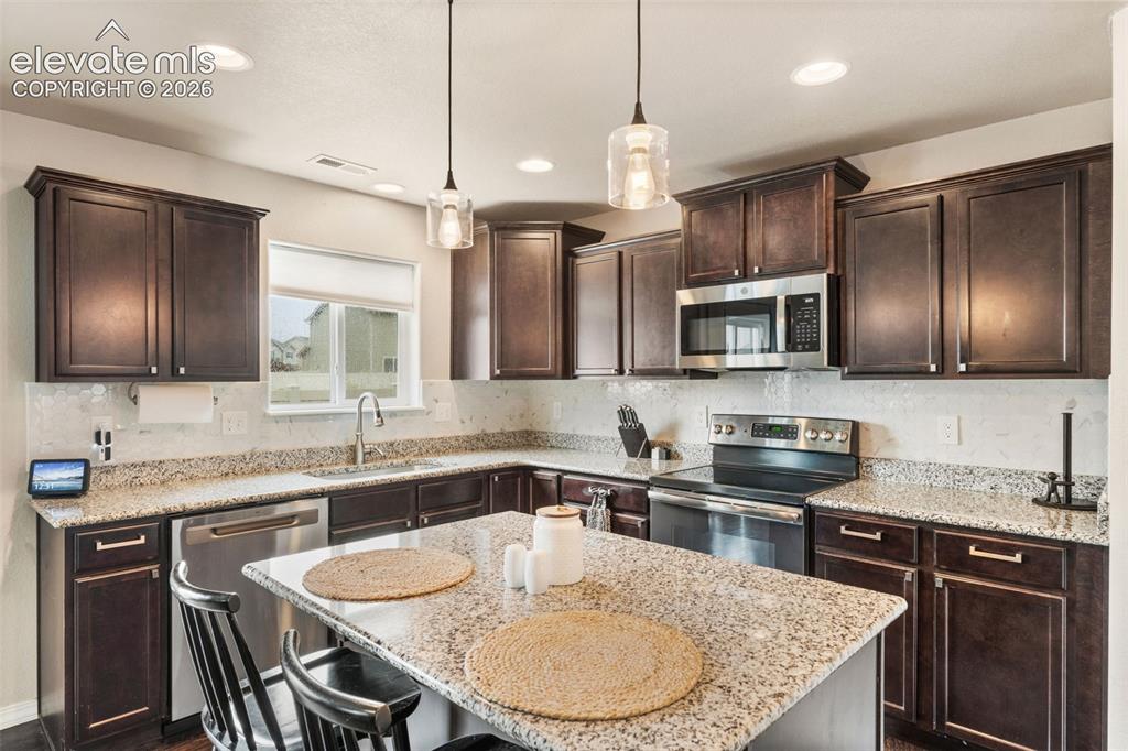 Image 17 of 42: Kitchen featuring dark wood cabinetry, light-toned countertops, stainless s
