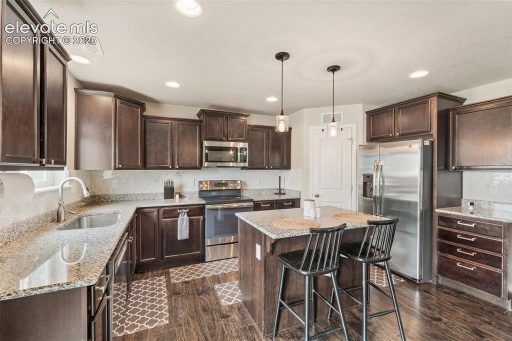 Image 2 of 42: Kitchen featuring wood-finish flooring, dark wood cabinetry, stainless stee