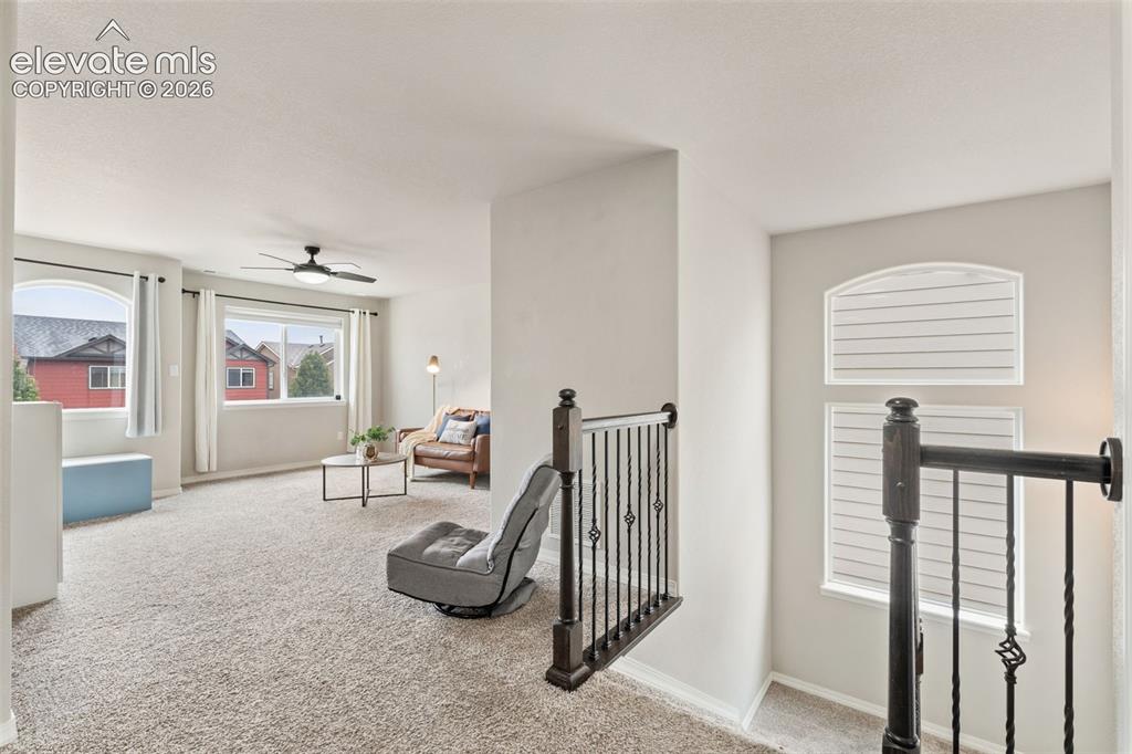 Image 20 of 42: Carpeted loft area with multiple windows, a ceiling fan, and wrought iron b