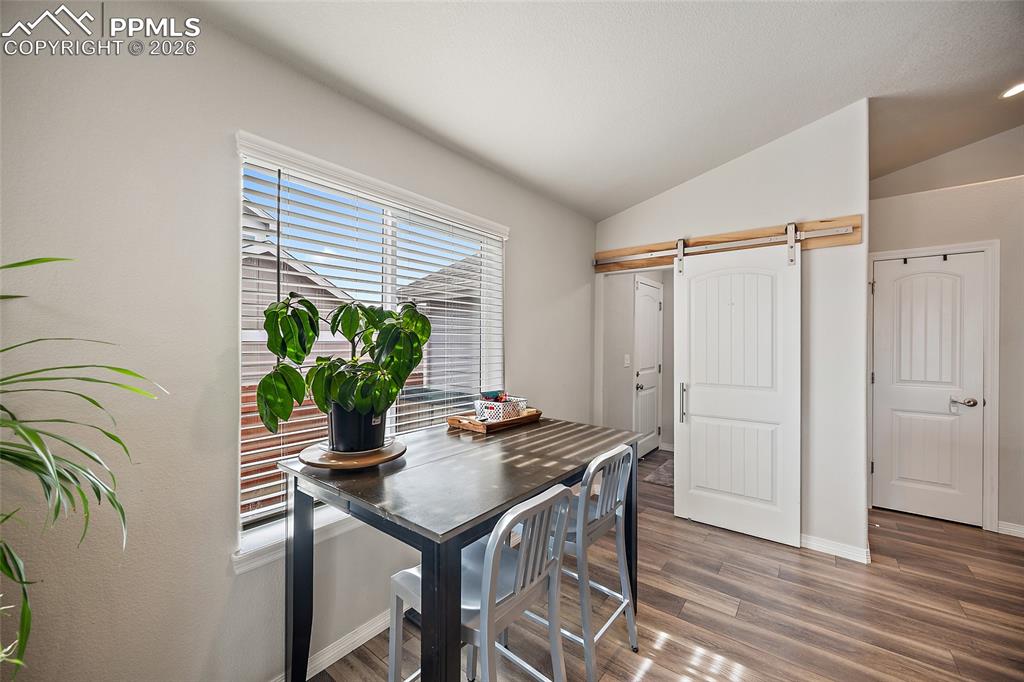 Image 16 of 43: Dining room with a barn door, vaulted ceiling, and wood finished floors