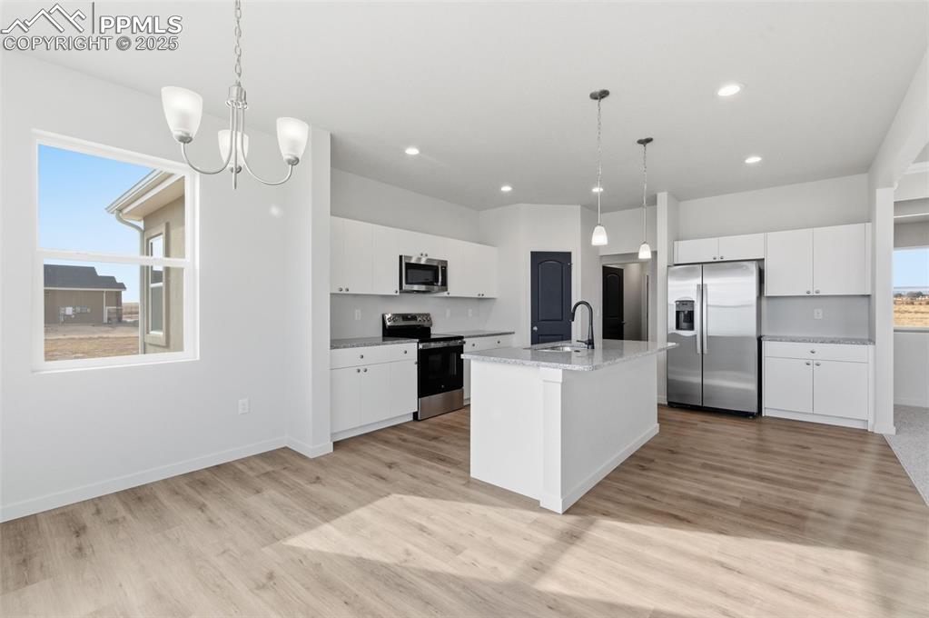 Image 12 of 26: Kitchen with white cabinetry, stainless steel appliances, decorative light
