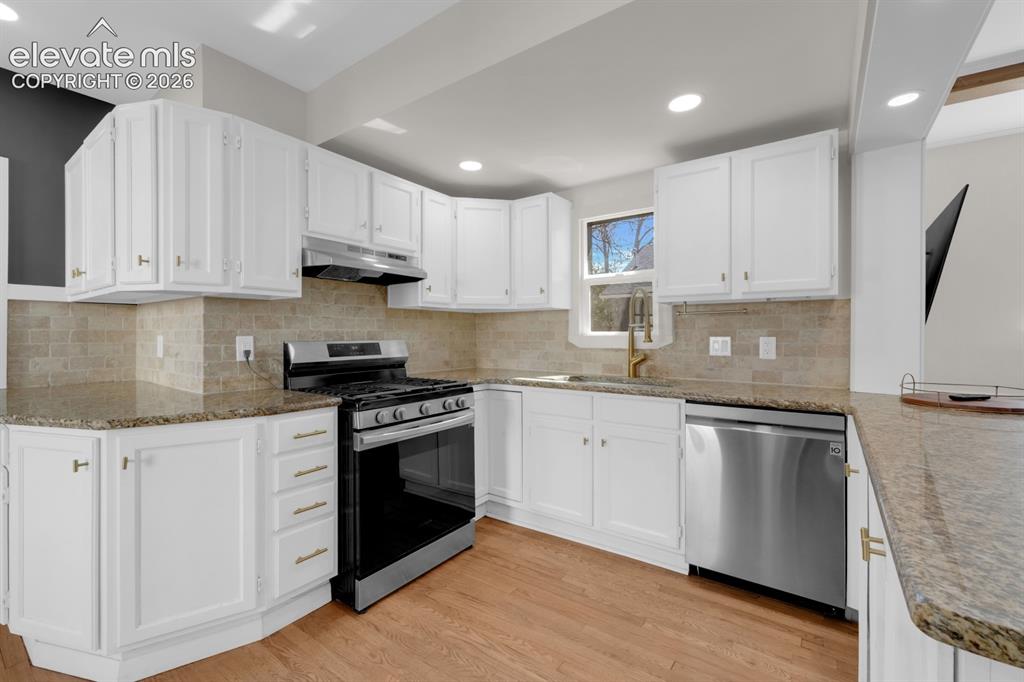Image 11 of 32: Kitchen featuring white cabinetry, stone-finish countertops, subway tile ba