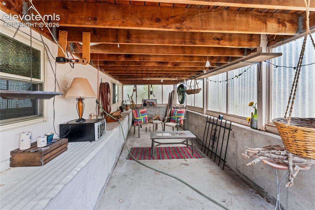 Image 20 of 46: Enclosed patio with exposed wood beam ceiling, concrete flooring, and trans
