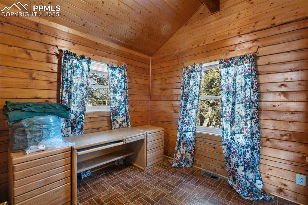Image 11 of 33: Bedroom with brick patterned flooring, wood walls, vaulted ceiling, and ple