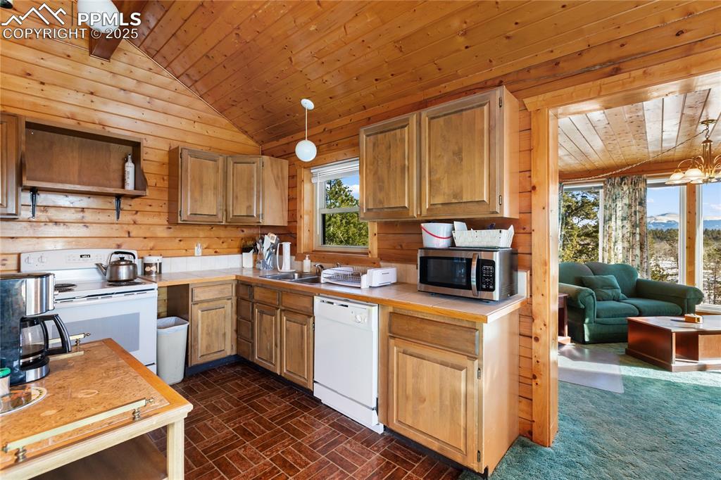 Image 14 of 33: Kitchen with white appliances, pendant lighting, wooden walls, wooden ceili
