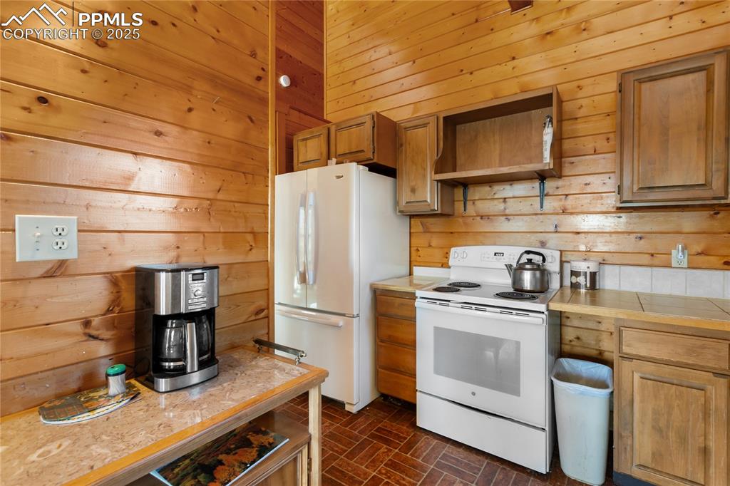 Image 15 of 33: Kitchen with wooden walls, white appliances, brick patterned flooring, bric