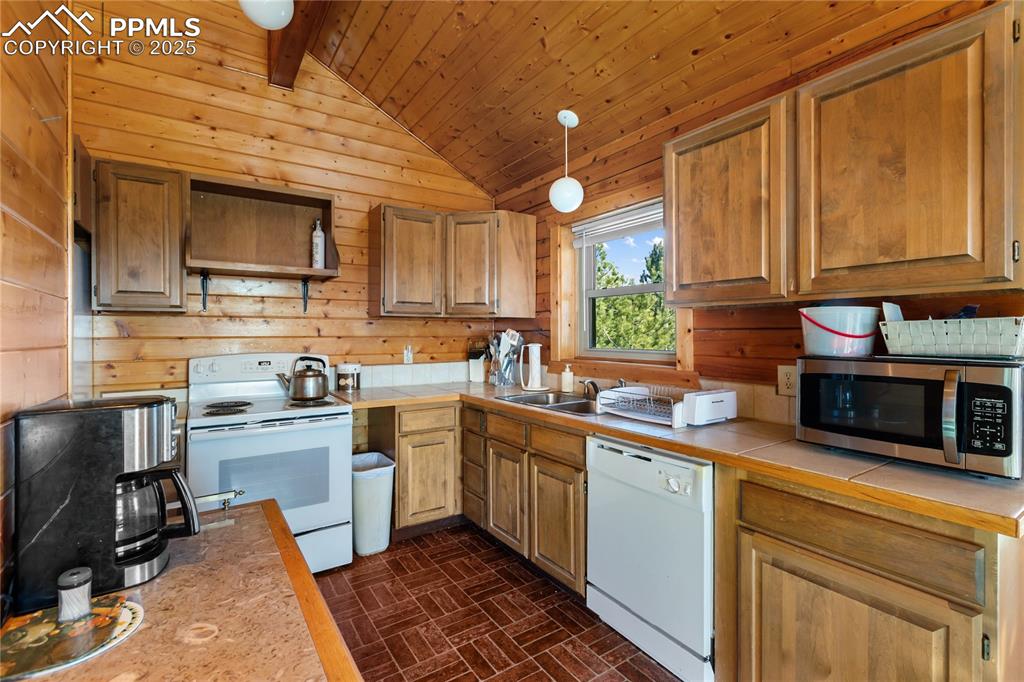Image 16 of 33: Kitchen featuring white appliances, brick patterned floors, wooden walls, b
