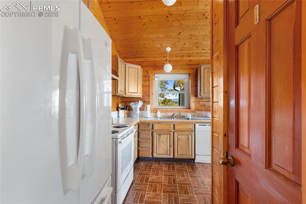 Image 17 of 33: Kitchen featuring white appliances, brick patterned floors, hanging light f