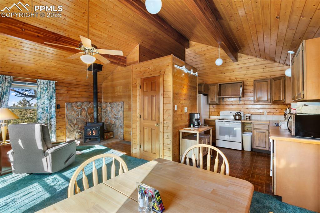 Image 18 of 33: Dining space with a wood stove, wooden walls, wooden ceiling, and ceiling f