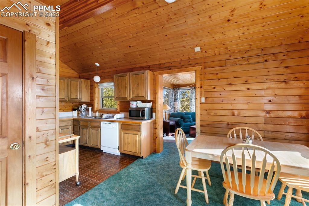 Image 19 of 33: Dining room and kitchen featuring wooden ceiling, wooden walls, white dishw