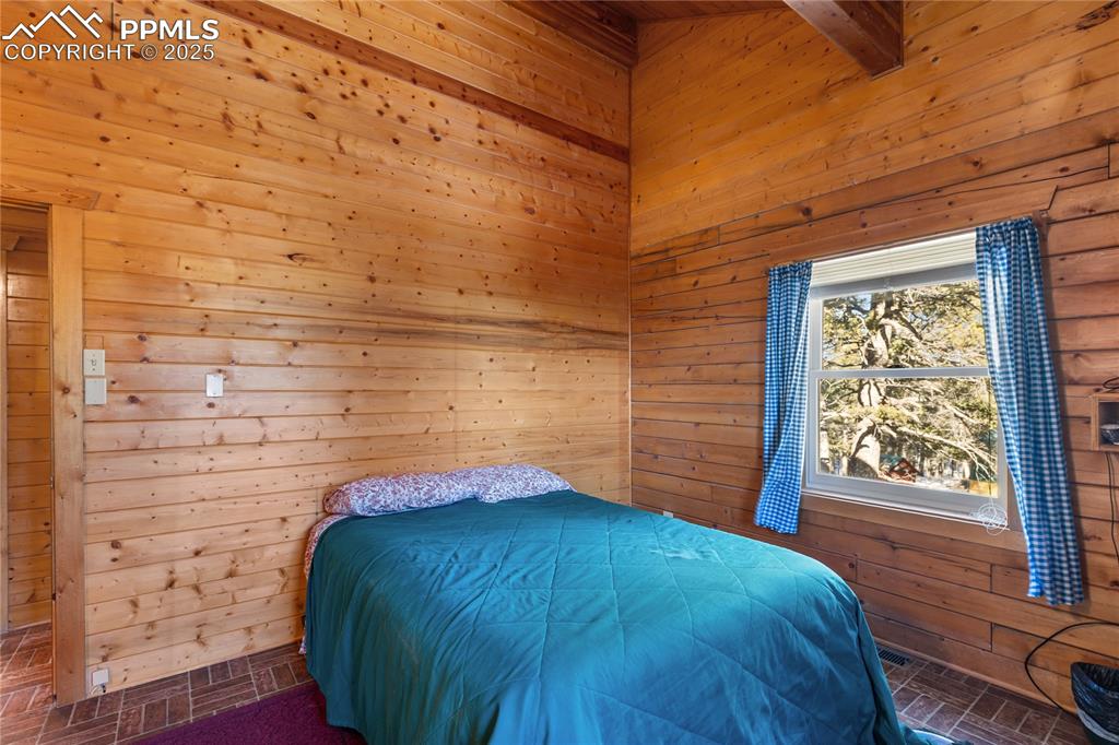 Image 24 of 33: Bedroom with brick patterned flooring and wood walls