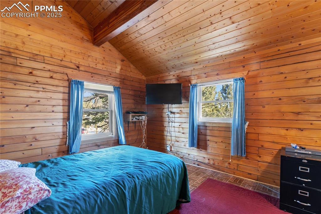 Image 25 of 33: Bedroom featuring wooden walls, wooden ceiling, and multiple windows