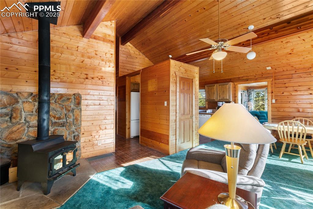 Image 7 of 33: Living room with a wood stove, wooden walls, wood ceiling, and a ceiling fa