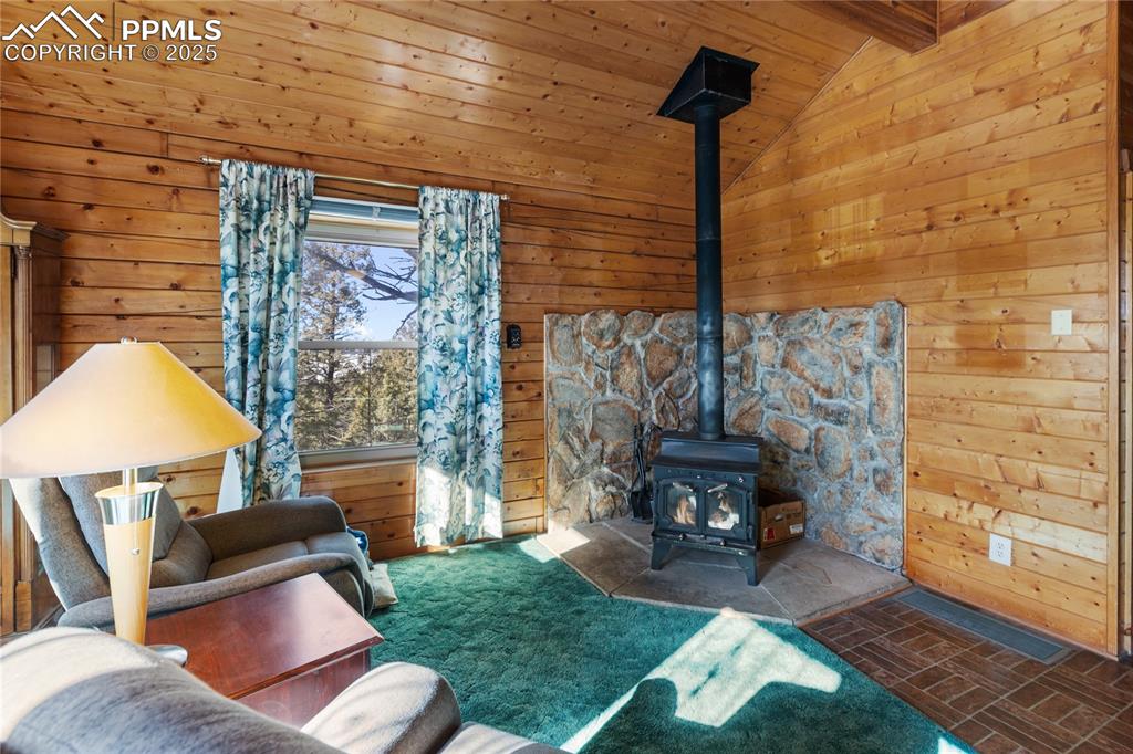 Image 8 of 33: Living room with a wood stove, wood walls, brick patterned flooring, and ca