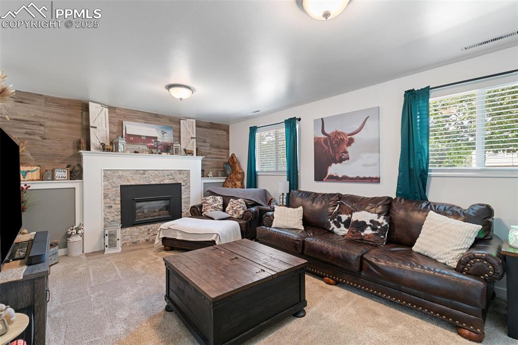 Image 12 of 45: Living room with wooden walls, light colored carpet, and a stone fireplace