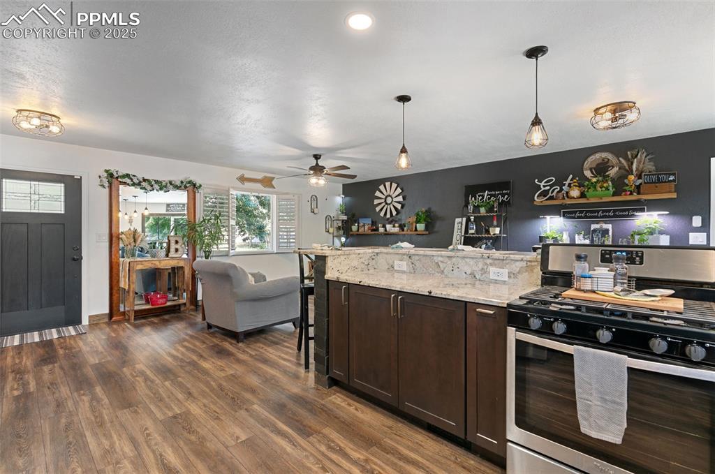 Image 9 of 45: Kitchen with gas stove, dark brown cabinets, light stone countertops, open 