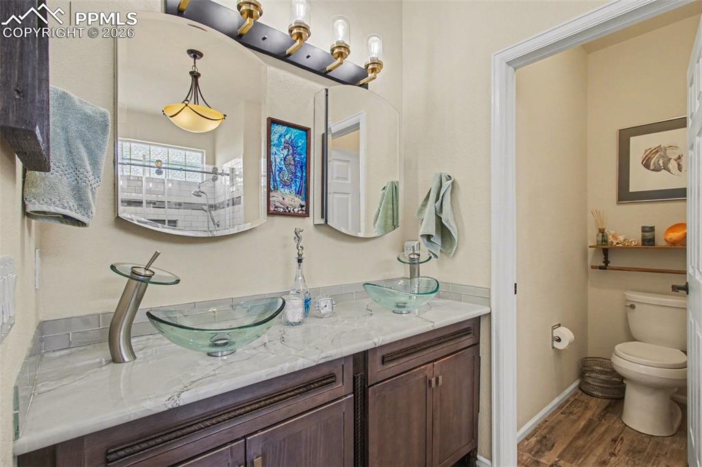 Image 19 of 42: Full bathroom with double vanity, dark wood-style floors, and tiled shower