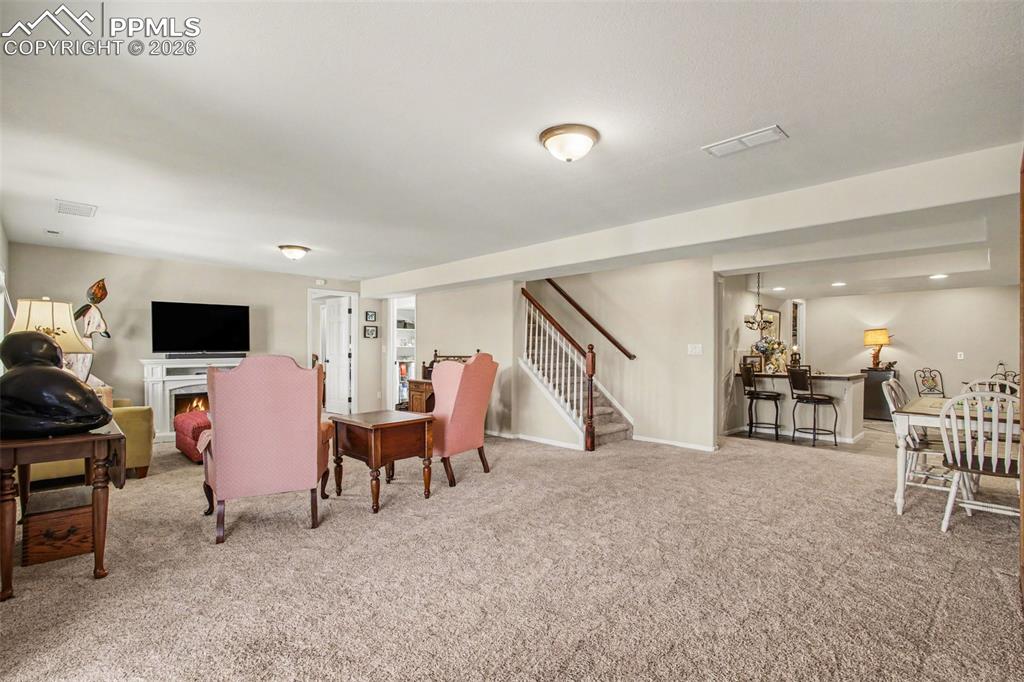 Image 26 of 42: Living area with light colored carpet, a lit fireplace, and recessed lighti