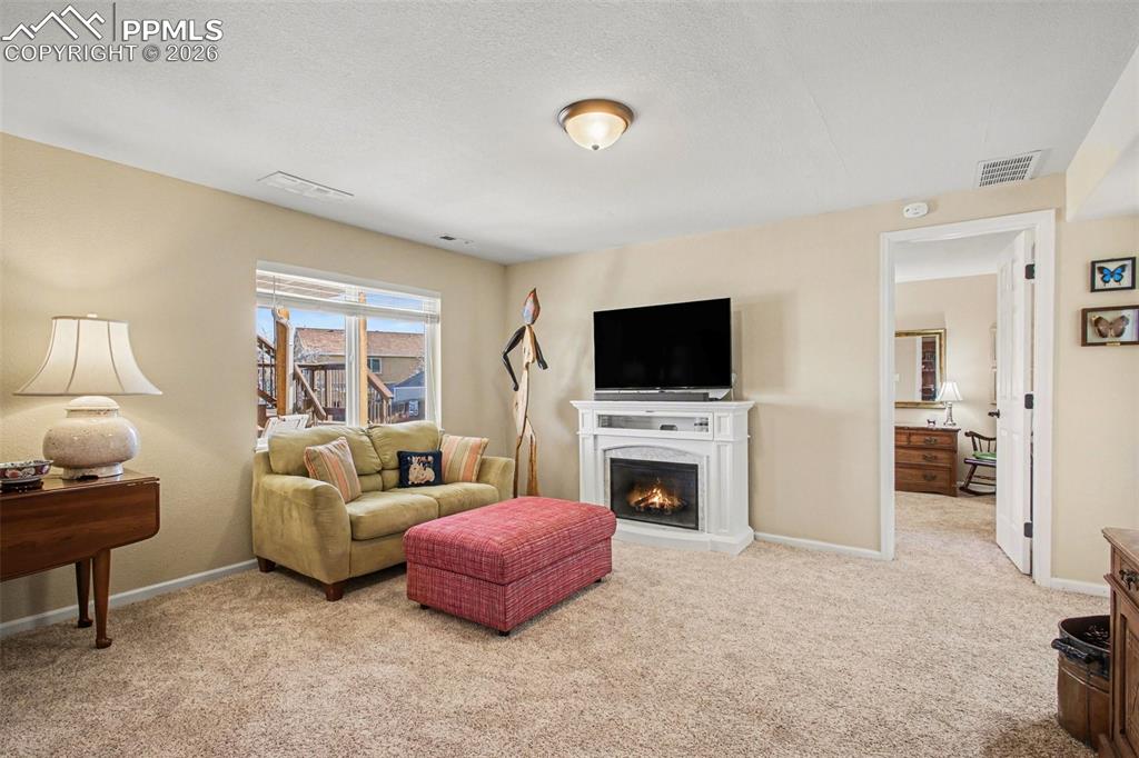 Image 27 of 42: Living area with a warm lit fireplace and light colored carpet