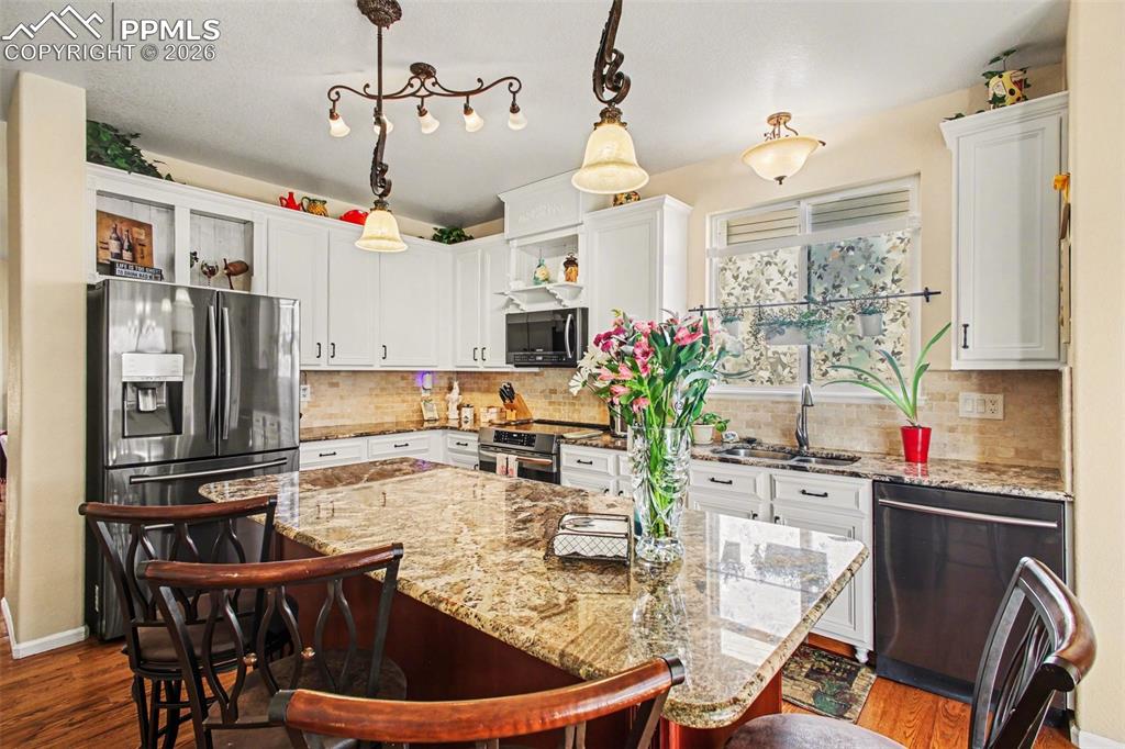 Image 9 of 42: Kitchen with light stone counters, white cabinets, a breakfast bar, a kitch