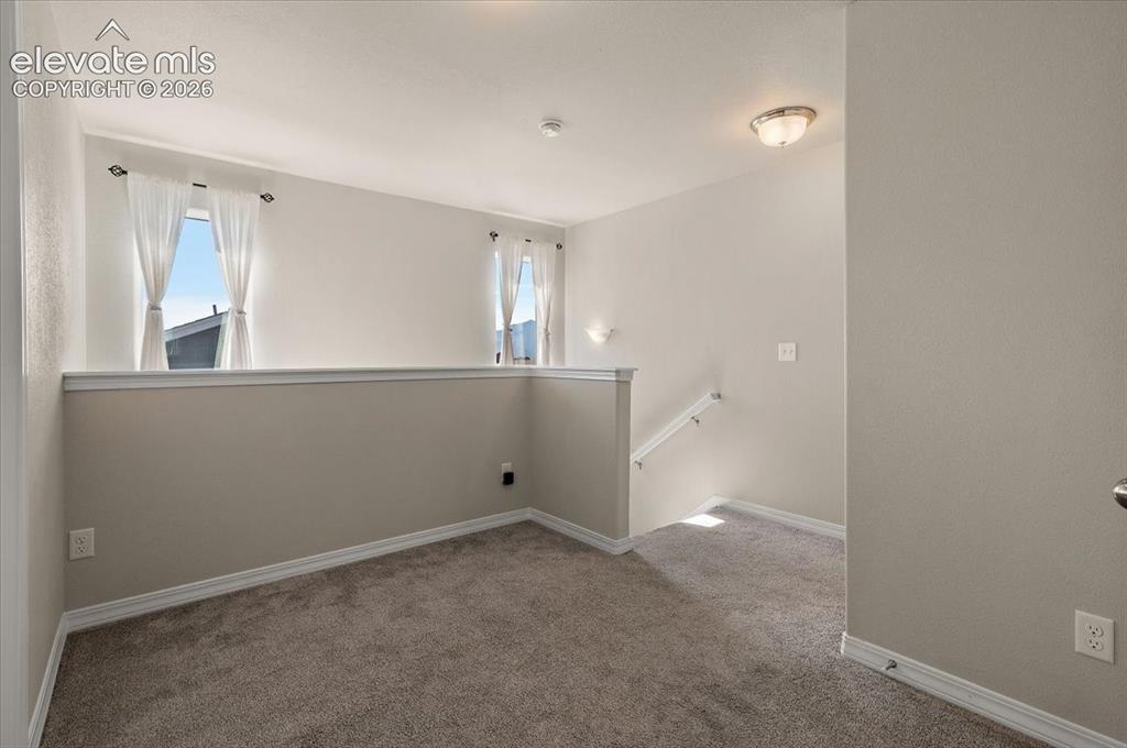 Image 27 of 31: Carpeted open loft area with a partial wall, two windows, and a flush-mount