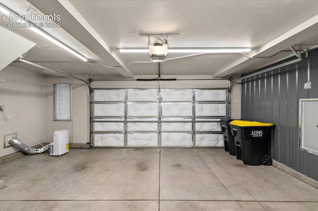 Image 28 of 31: Concrete flooring, overhead strip lighting, insulated garage door, corrugat