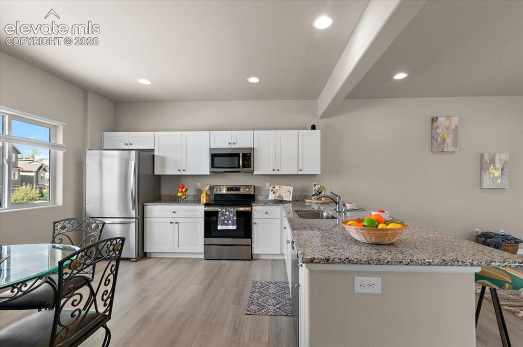 Image 7 of 31: Kitchen featuring wood-finish flooring, white cabinetry, stainless steel ap