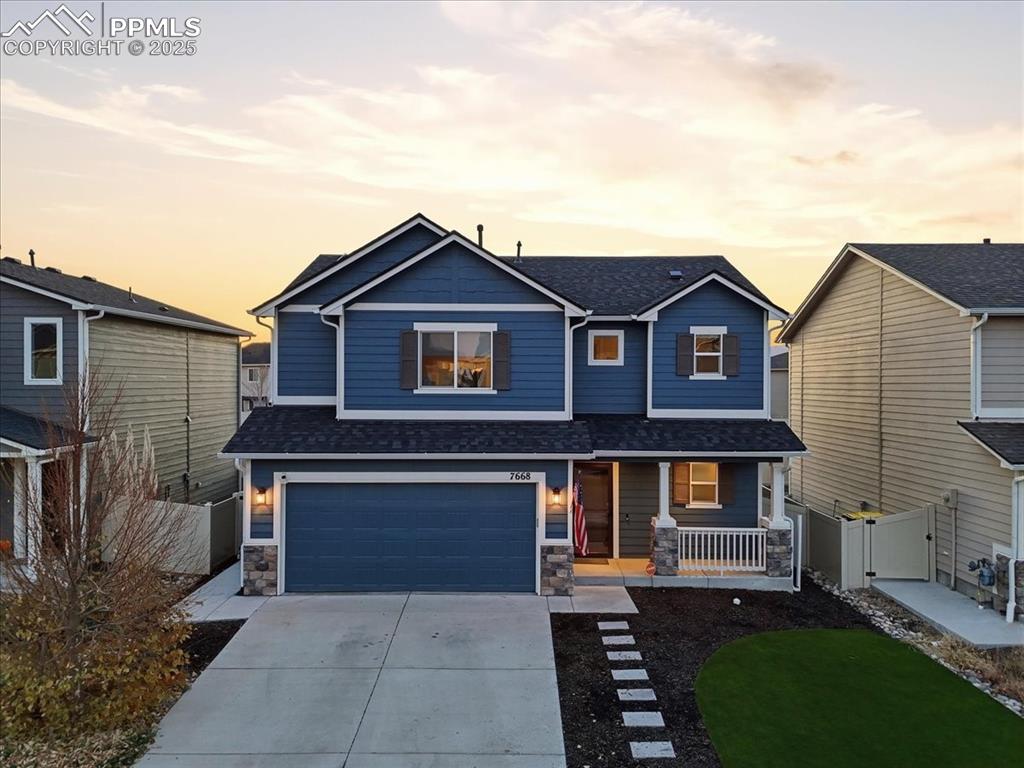 Caption: View of front of house featuring covered porch, stone siding, roof with shingles, concrete driveway,