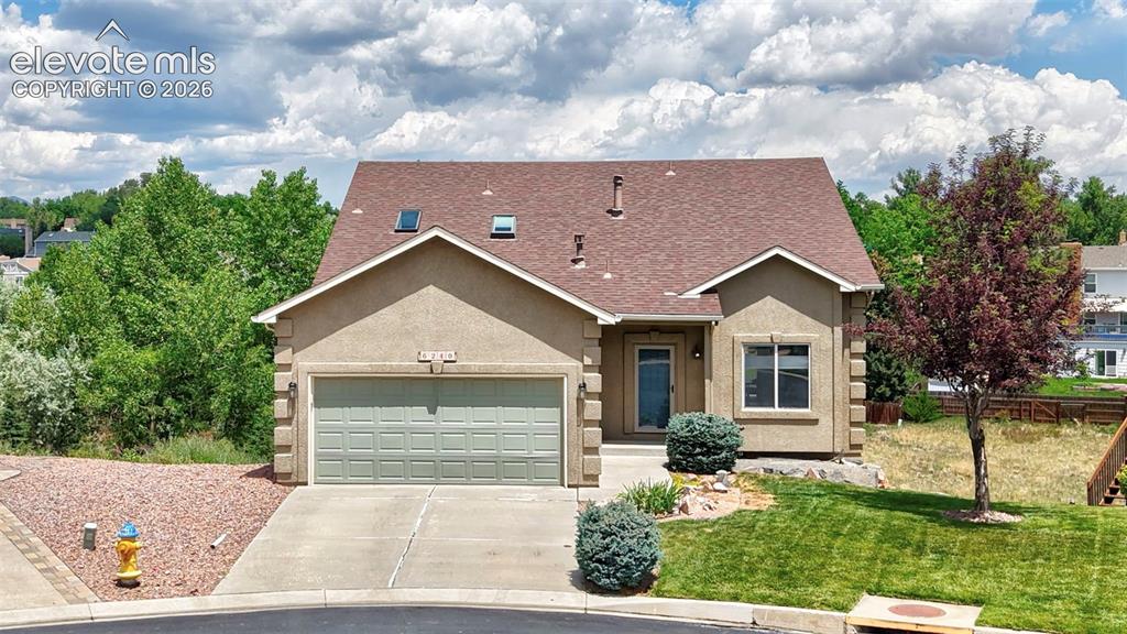 Image 2 of 50: Multi-level residence featuring a two-car garage, front lawn, and mature la