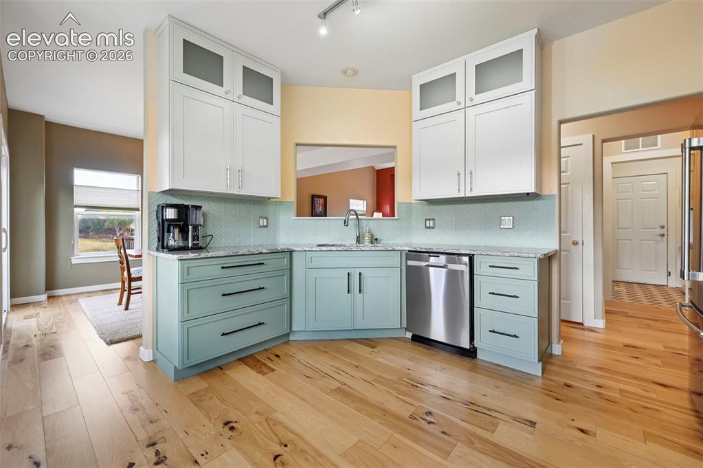 Image 24 of 50: Kitchen featuring light wood-finish flooring, two-tone cabinetry with upper