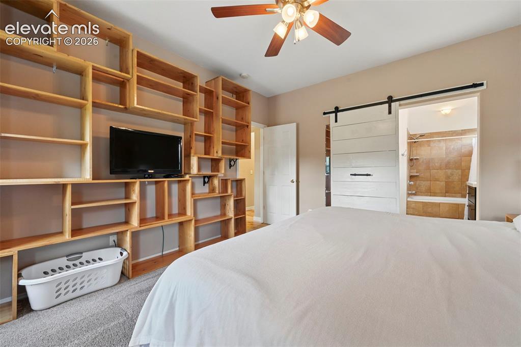 Image 29 of 50: Custom wood-finish shelving unit, wood-finish ceiling fan, gray carpet floo