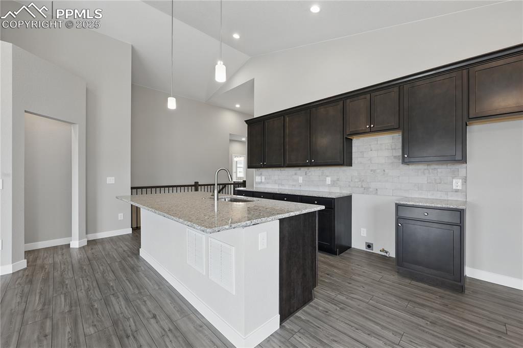 Image 15 of 35: Kitchen with a sink, dark brown cabinetry, light stone countertops, vaulted