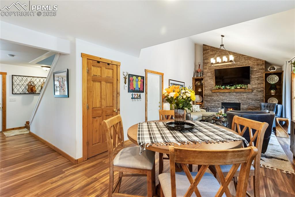 Image 30 of 50: Dining space with wood finished floors, a stone fireplace, and vaulted ceil