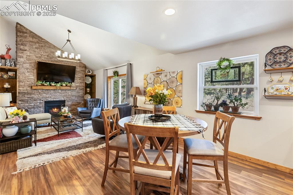 Image 33 of 50: Dining space with wood finished floors, a stone fireplace, and vaulted ceil