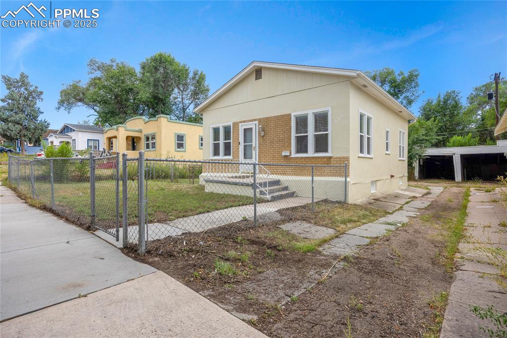 Image 2 of 28: Bungalow featuring brick siding, a fenced front yard, and stucco siding