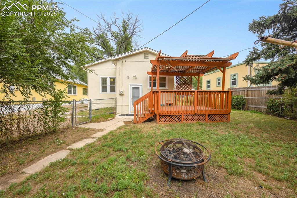 Image 22 of 28: Back of house featuring a fenced backyard, a wooden deck, a gate, a fire pi