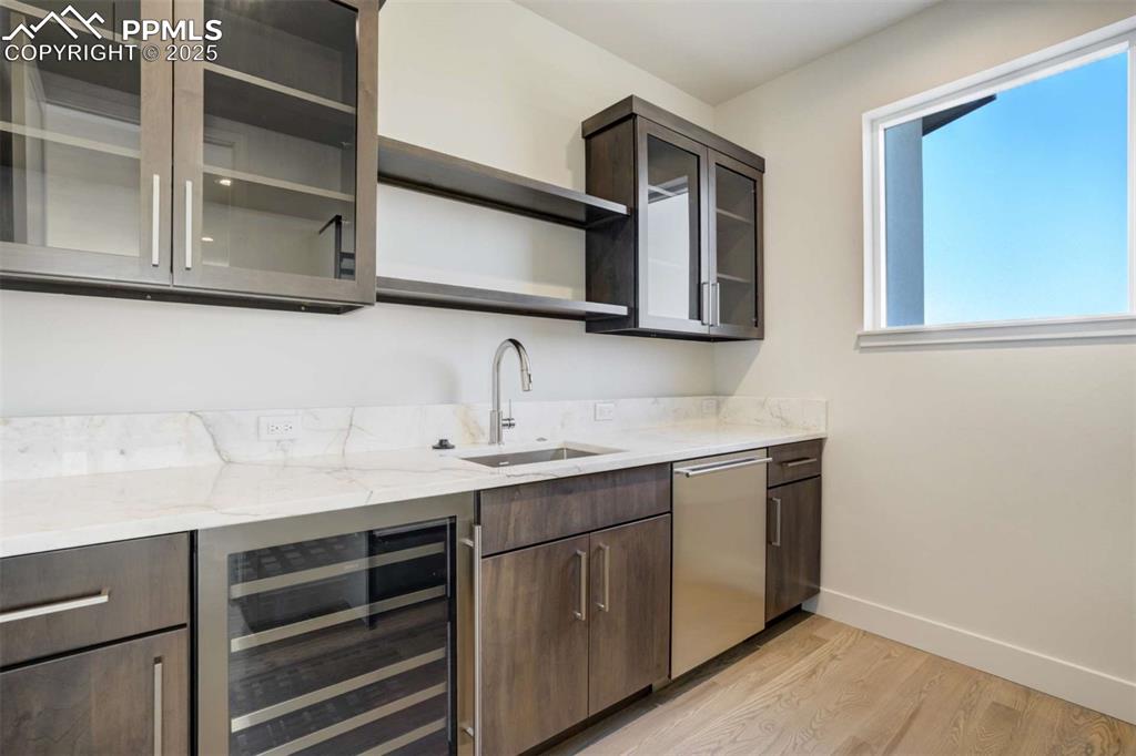 Image 10 of 34: Bar with open shelves, light wood-type flooring, wine cooler, light stone c